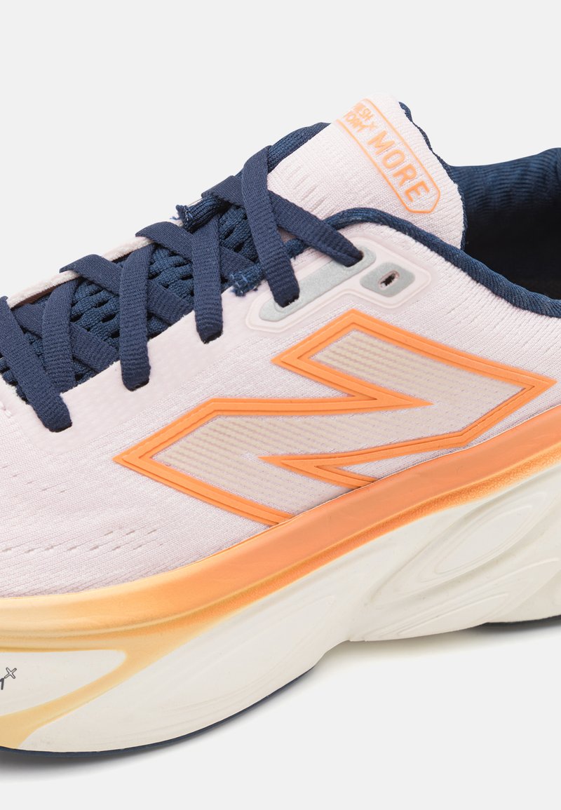 Zapatilla de color morado claro con acentos naranjas, cordones en azul marino y tela texturizada. Presenta una suela blanca gruesa con detalles de patrón esculpido.