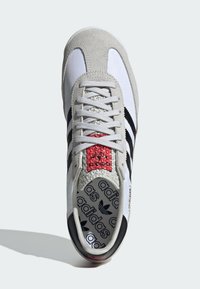 Grijze suede en witte textiel sneakers met zwarte strepen, rode accent op de tong, patroon op de binnenzool en een gestructureerde buitenzool. Veters zijn grijs.