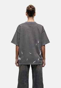 Szara, przewiewna koszulka z okrągłym dekoltem i krótkimi rękawami, z białymi akcentami plam farby. Miękka tkanina o luźnym kroju.