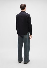 Must pikkade varrukatega must särk koos kraega, koos laia lõikega siniste teksadega. Kampsunil on tekstureeritud kangas ja nööpidega mansetid.