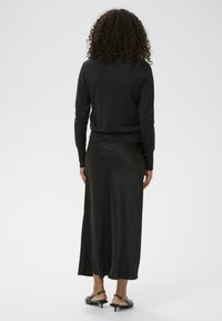 Suéter de punto negro combinado con una falda larga de satén negra. El conjunto tiene una textura suave y una silueta ajustada, con acentos sutiles.