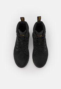 Las botas de gamuza negras hasta el tobillo presentan cordones redondos y una suela de goma duradera. La lengüeta tiene una marca amarilla y el interior está acolchado para mayor comodidad.