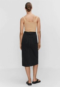 Černá džínová midi sukně se dvěma zadními kapsami, vysokým pasem, doplněná béžovým žebrovaným tílkem. Hladká textura, ležérní styl.
