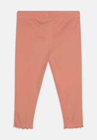 Ribbad leggings i en mjuk persikofärg med en åtsittande design och vågkant. Tillverkade av stretchtyg för komfort och flexibilitet.