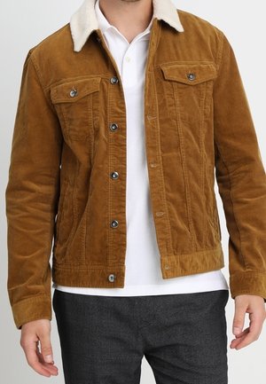 Bruine ribfluwelen jas met een crèmekleurige schapenvacht kraag, voorzien van twee borstzakken en knoopsluiting, textuurstof met ribbels.