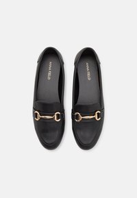 Des mocassins noirs en cuir lisse avec un accent en matériel doré et un bout arrondi. L'intérieur présente un doublage doux.