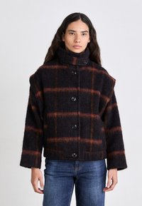 Giacca in misto lana con colletto alto, caratterizzata da un ampio motivo a quadri in toni scuri con accenti arancioni e sei bottoni sul davanti.
