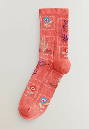 Calcetines coral con un patrón completo que presenta flores, cactus y sombreros en colores brillantes, tejido texturizado y detalle en la puntera de color contrastante.