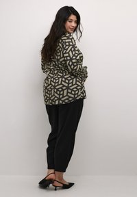 Musterhemd in beigem und schwarzem geometrischem Druck, kombiniert mit schwarzen, schmal zulaufenden Hosen und schwarzen Slingback-Absätzen. Strukturierte Stoffoberfläche.