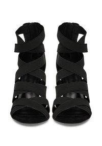 Mustade kõrge kontsaga sandaalid, millel on ristuvad kangastrapid ja avatud varvas. Tekstuuriga viimistlus ja tagumine tõmblukk kindla istuvuse tagamiseks.