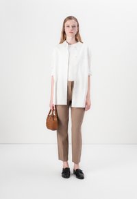 Bílá košile na knoflíky přes přiléhavý krémový top, hnědé dobře padnoucí kalhoty a malá pletená hnědá kabelka. Celý outfit doplňují černé ploché boty.