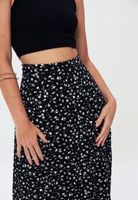 Falda negra con estampado floral en blanco, de cintura alta y tejido fluido. Combinada con un top corto negro de canalé, de textura suave.