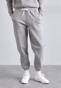 Grå sweatpants med elastisk midja och muddar, med dragsko. Bärs med vita sneakers och strumpor. Slät textur och avslappnad design.