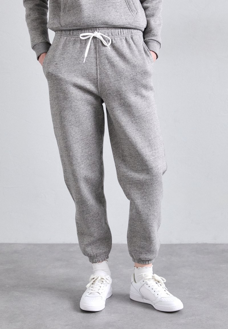Grå sweatpants med elastisk midja och muddar, med dragsko. Bärs med vita sneakers och strumpor. Slät textur och avslappnad design.
