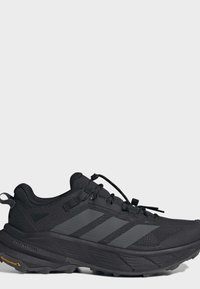 Chaussure de trail running Adidas Terrex noire avec semelle texturée, trois bandes sur le côté et système de laçage rapide sur fond gris.