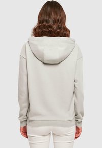 Világosszürke kapucnis pulóver, puha tapintással, zsinóros kapucnival, bordázott ujjal és aljjal, hátulról nézve. Minimalista dizájn, minta nélkül.
