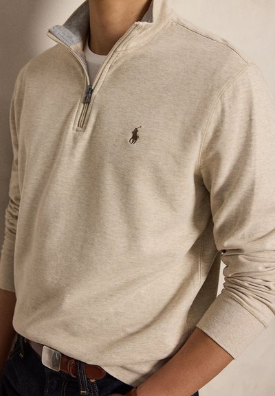 Beige trui met lange mouwen, een kwart ritssluiting en een klein geborduurd polo speler logo op de linkerborst.
