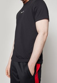 Mustat puuvillaiset T-paidat lyhyillä hihoilla ja pyöreällä kaula-aukolla. Tässä on pieni kultainen logo rinnassa ja kapea siluetti.