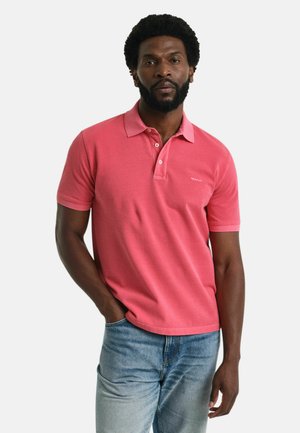 Camisa polo en tejido coral con cuello clásico, mangas cortas y un logo sutil en el pecho; combinada con jeans de color azul claro.