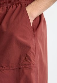 Bordeaux shorts med elastisk talje, sidelommer og et broderet Jumpman-logo på den nederste venstre side. Glat tekstur.