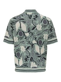 Chemise à manches courtes avec motifs floraux et feuillages abstraits en vert, gris, noir et blanc, avec bordure en zigzag aux manches et à l'ourlet.