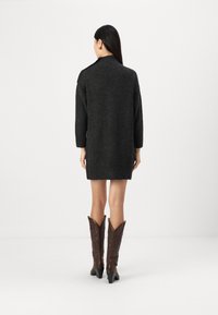 Robe en laine gris foncé avec un col haut et des manches longues, présentant une coupe ample et des fentes latérales, associée à des bottes de style cowboy marron.