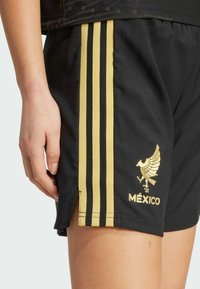 Shorts sportivi neri con strisce dorate e un emblema d'aquila dorato. Il materiale sembra leggero e ha una consistenza liscia.