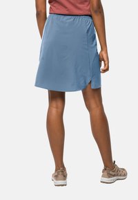 Blauwe sportrok met een elastische tailleband, zijsplit en een gladde textuur, gecombineerd met lichtbruine sportieve schoenen.