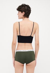 Top corto nero a coste con spalline sottili abbinato a pantaloni corti verde oliva caratterizzati da una cintura bianca con il logo "BJÖRN BORG". Vista posteriore.