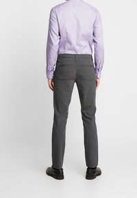 Šedé kalhoty na míru se slim fit střihem, dvěma zadními kapsami, nošené s dlouhým světle fialovým tričkem a černými botami.