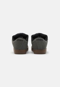 Sneakers in suède grigio con rivestimento in tessuto nero, tallone a fantasia e suola in gomma marrone. Presentano il marchio "etnies" sul tallone.