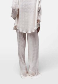 Leichtes, transparentes Oberteil und passende Hose in Off-White mit dezem vertikalen Streifenmuster. Das Oberteil hat einen gerüschten Saum und die Hose hat einem weiten Schnitt.