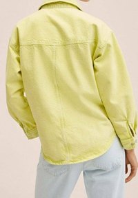 Camicia in denim verde lime con colletto a bottoni, maniche lunghe e orlo arrotondato. Cuciture in vista e dettagli di texture sottili in tutto il capo.