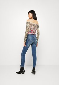 Top off-the-shoulder con stampa leopardata e dettagli floreali, abbinato a jeans skinny blu e stivaletti neri, che evidenziano un design aderente.