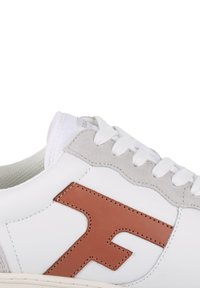 Sneaker bianco con un accento in pelle marrone, dettagli in suede grigio sul tallone e lacci bianchi. Linguetta strutturata e design del logo laterale.