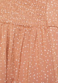 Tecido leve de cor pêssego com bolinhas brancas. Apresenta um topo franzido com pregas gathered, realçando a textura e o fluxo.