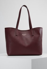 Bordeauxrode nepleren totebag met dubbele schouderbanden, voorzien van een gladde buitenkant en een geperst "GUESS"-logo aan de voorkant.