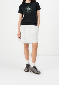 Camiseta de algodón negra con estampado gráfico verde; falda de mezclilla blanca con bolsillos; zapatos de senderismo grises con cordones negros y calcetines blancos.