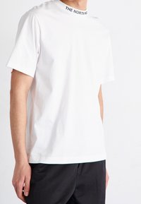 Biała bawełniana koszulka z okrągłym dekoltem, z czarną bandą z logo. Krótkie rękawy i prosty krój, zestawiona z ciemnymi spodniami.