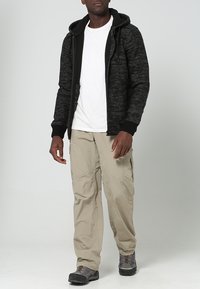 Svart och grå hoodie med snoddar, vit t-shirt under, ljusbeige cargobyxor och svarta vandringskängor.