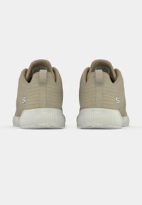 Beżowe buty sportowe z teksturowaną cholewką, pętelką z tyłu i gumową podeszwą. Z widocznym logo po boku.