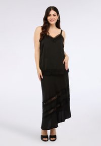 Vestito nero con spalline sottili, bordo in pizzo, design a strati e orlo asimmetrico. Tessuto morbido e fluente con dettagli in pizzo trasparente.