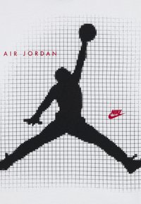 Λευκό T-shirt με μεγάλη μαύρη σιλουέτα άλματος, κείμενο «AIR JORDAN» σε κόκκινο και κόκκινο λογότυπο Nike. Σχέδιο φόντου με πλέγμα.