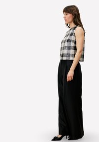 Zwart-witte geruite mouwloze top gecombineerd met hooggetailleerde zwarte broek, met een losse pasvorm en subtiele glans.