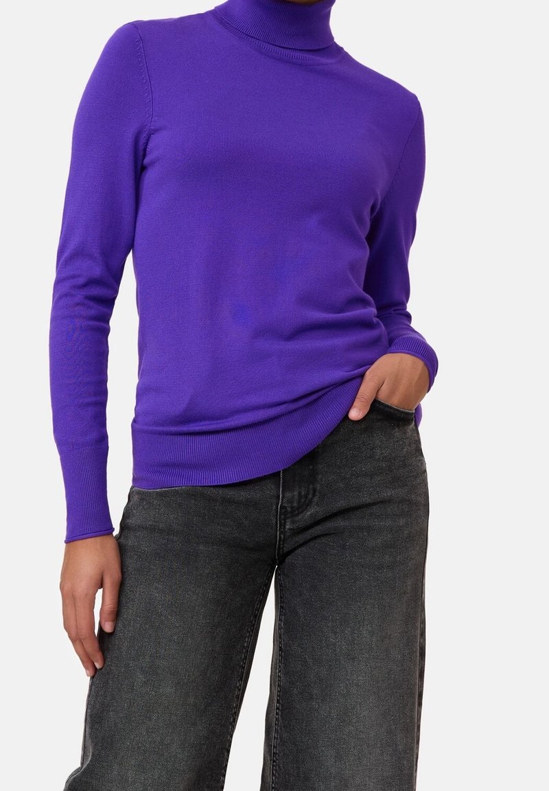 Pull col roulé violet en tricot doux, avec des manches longues et une coupe ajustée, associé à un jean gris foncé.