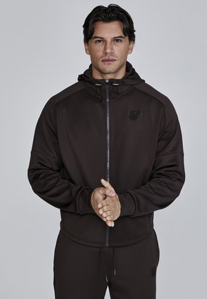 Dark brown zip-up hoodie with a hood, featuring a front pocket and logo detail on the chest. Made from smooth, stretchy fabric.