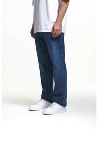 Niebieskie dżinsy z denimu o luźnym kroju, z podwiniętymi nogawkami i przednimi kieszeniami. Połączone z białymi trampkami, noszone z luźną białą koszulką.