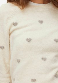 Pull en maille crème avec motifs en forme de cœur texturés gris, col rond et tissu doux en mélange de laine.