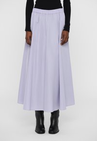 Lys lilla lang skjørt med elastisk midjebånd, med en flytende design og minimal tekstur, parret med svarte ankelstøvler.
