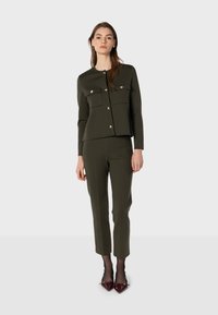 Olive green saková bunda so dvěma náprsními kapsami a stříbrnými knoflíky, spárovaná s úzkými kalhotami ve stejné barvě a vínovými lakovanými lodičkami.
